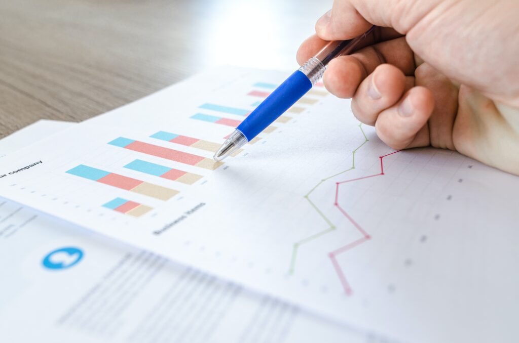 Como investir em Fiis: Vemos uma caneta azul e uma mão que a segura sobre uma folha contendo gráficos e análises.