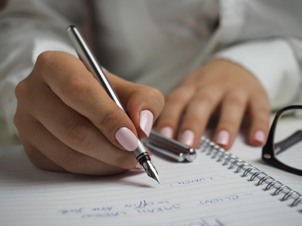 Fundos de fundos: Mãos segurando uma caneta enquanto escreve em um caderno de arame.