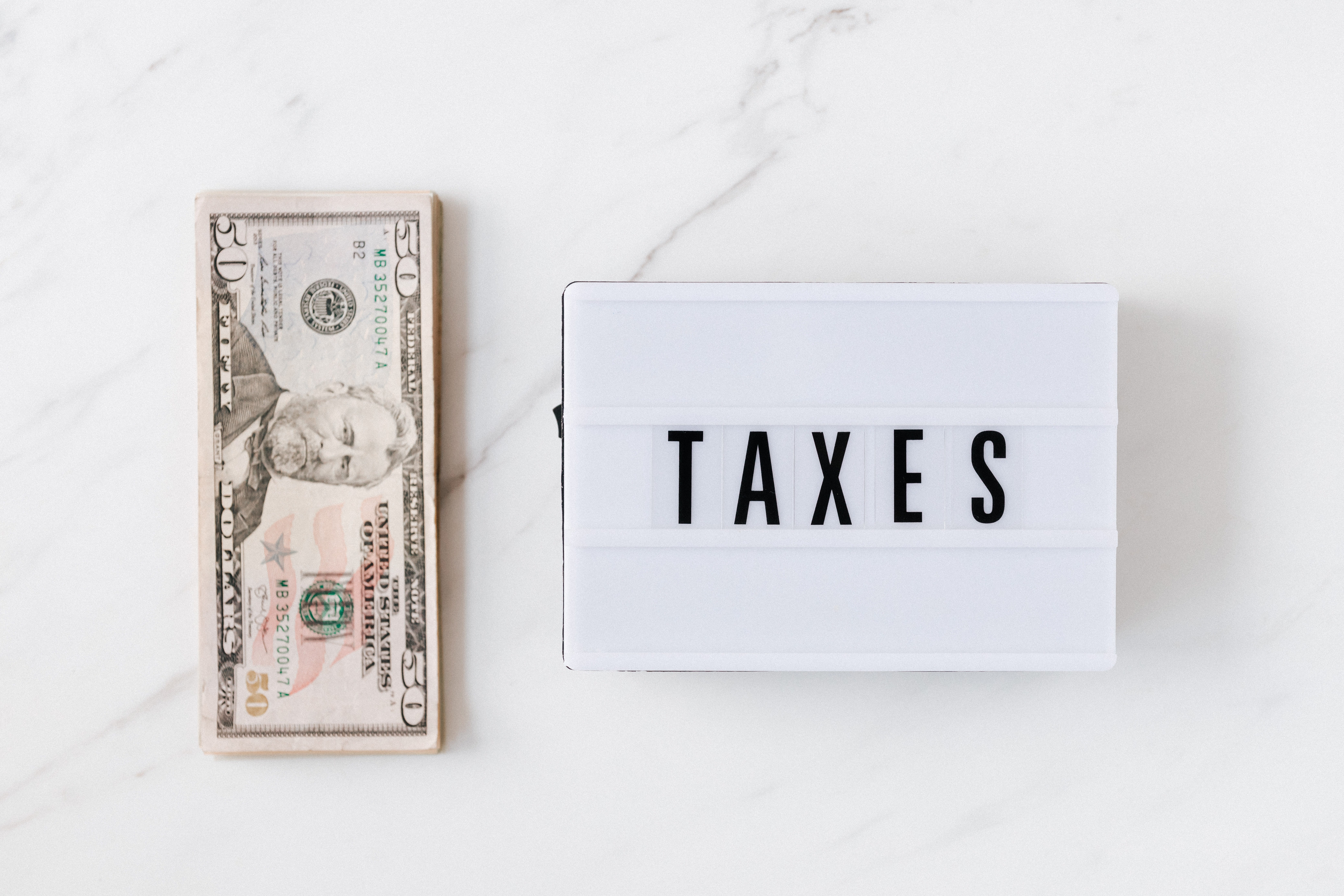 Imposto de Renda dos Fiis: Vemos um malote de dólares e ao lado um pequeno letreiro com a palavra "Taxes"