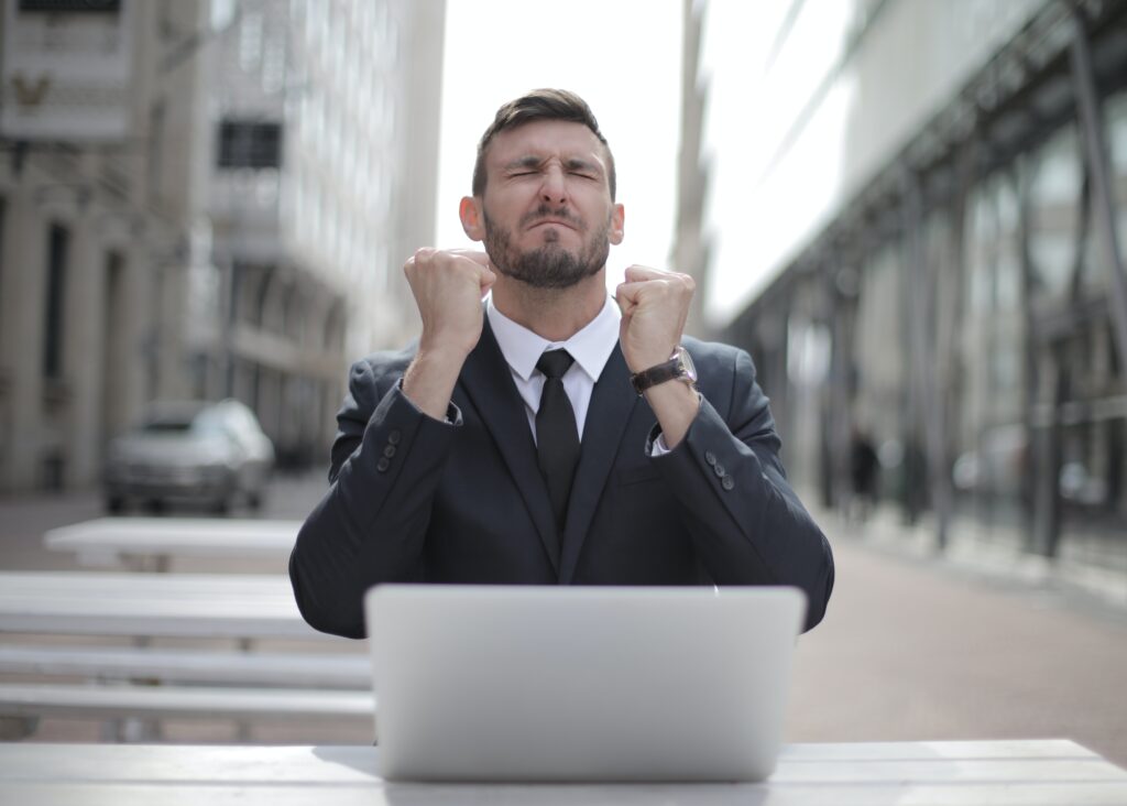 Investir em Fiis: Vemos um homem de terno comemorando de olhos fechados de frente para um laptop.