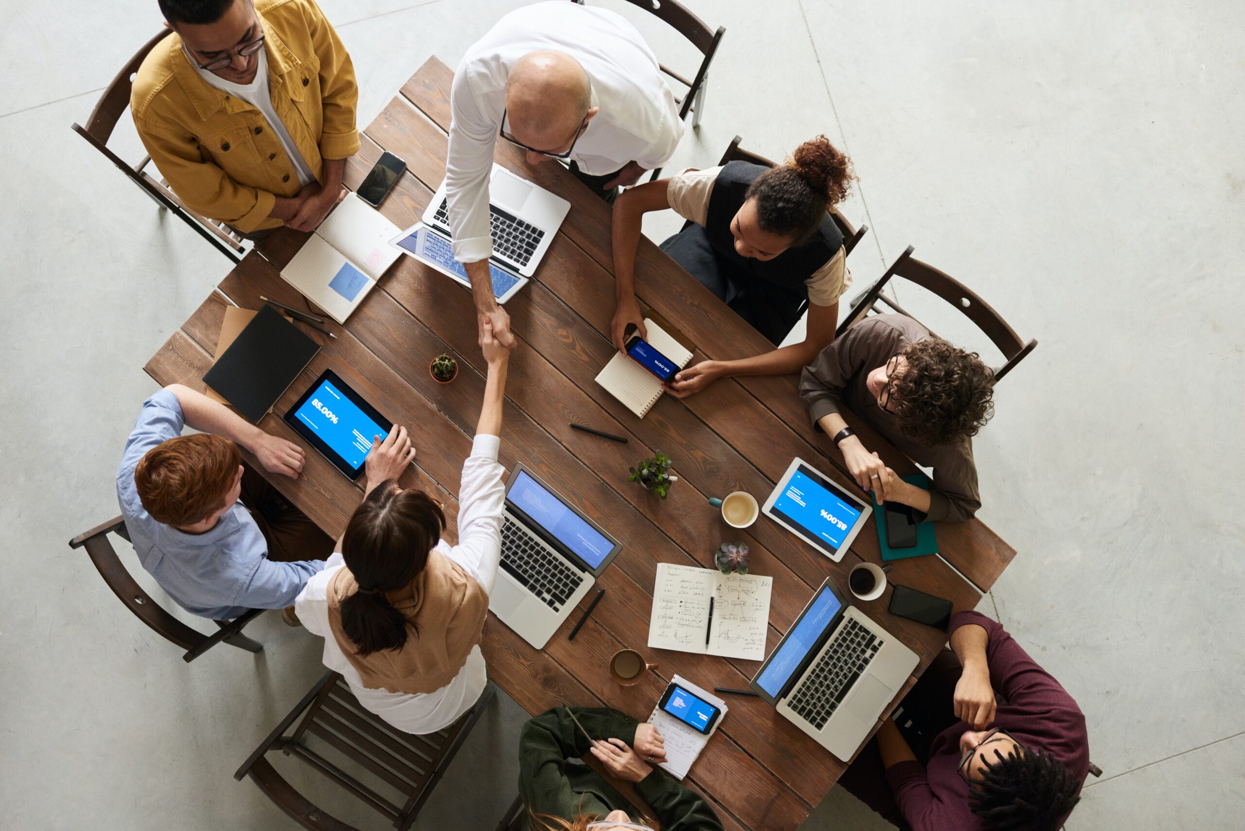 Vemos pessoas em reunião com laptops e cadernos enquanto duas dessas pessoas dão um aperto de mão, remetendo ao investidor profissional.