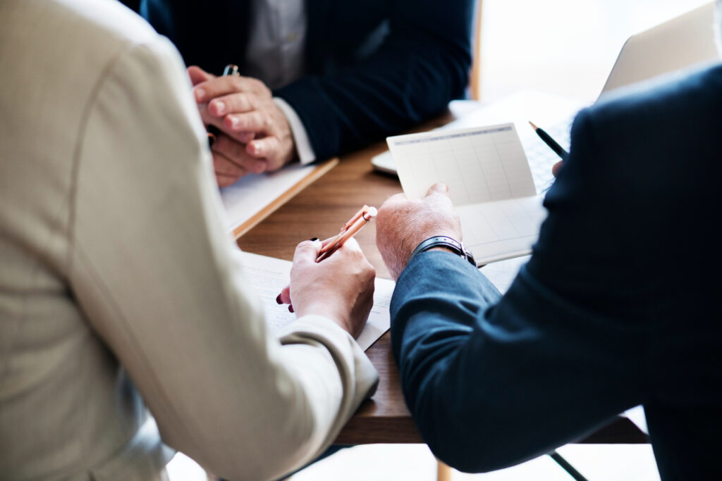 Três pessoas aparecem sentadas em uma mesa segurando vários papéis, como se estivessem decidindo um voto devido a uma ação ordinária de suas carteiras de investimentos.