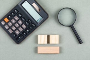 Calculadora, uns blocos de madeira e uma lupa estão sobre uma mesa para sinalizar o cálculo de rendimento das cotas