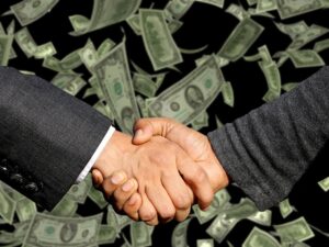 Executivos apertam as mãos em frente a várias notas de dólar mostrando o lucro líquido de uma empresa