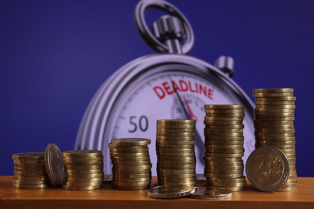 6 pilhas de moedas em ordem crescente aparecem em frente a um relógio mostrando o deadline do pagamento dos passivos