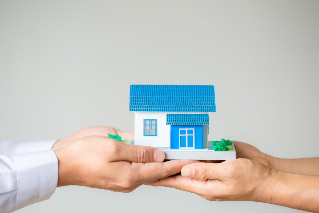 Mão de um executivo entrega uma casa em miniatura na mão de outra pessoa representando o SLB